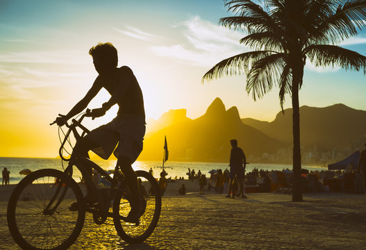 Scenic sunset view of unrecognizable cyclist riding his bike along the Ipanema Beach promenade in Rio de Janeiro, Brazil 