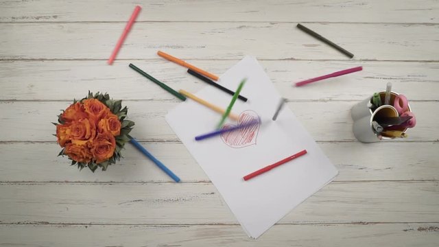 Colored pencils fall on a stylish white wooden table. Clow mo. Top view. Hands close up view. St. Valentine's Day