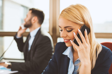 Young businesswoman talking on the phone with business man in the background in the office