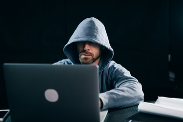 a man a hacker in a sweatshirt with a hood sits behind a laptop and then he poesetsya