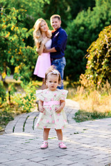 young happy family with little beautiful baby with blue eyes walking in summer park at sunset