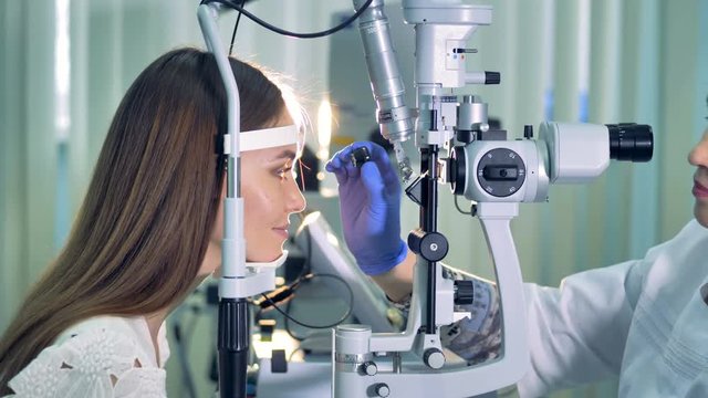 An ophthalmologist begins an exam on a young woman in the clinic. 