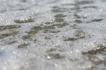 Fototapeta na wymiar Calm wave witn foam on the beach. Close up view. Selective focus. Copy, negative space. Natural texture background