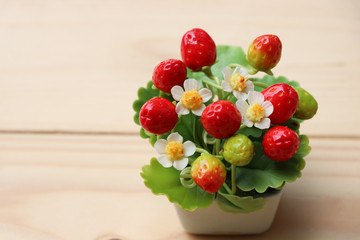 Artificial Strawberry Flowers with leaves in flower pot on wood background