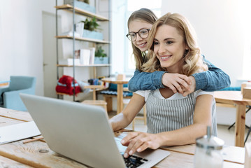 Warm atmosphere. Charming girl feeling happiness while embracing her mother and helping at work