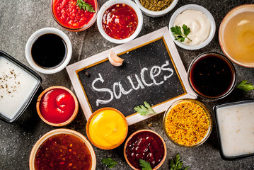 Set of different sauces - ketchup, mayonnaise, barbecue, soy, teriyaki, mustard, grain hills, pesto, adzhika, chutney, tkemali, pomegranate sauce on black stone background. Copy space