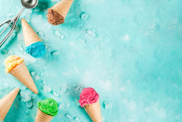 Selection of various bright multicolored ice-cream in ice cream cones - chocolate vanilla blueberry strawberry pistachio orange, on light blue sunny background, copy space top view
