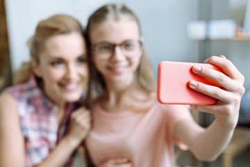 Pose on smartphone. Two female persons expressing positivity and standing close to each other while looking forward
