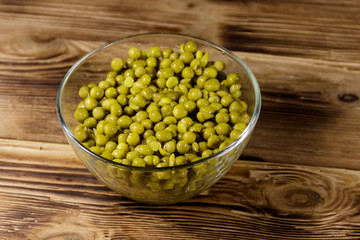 Canned green peas in glass bowl on wooden table