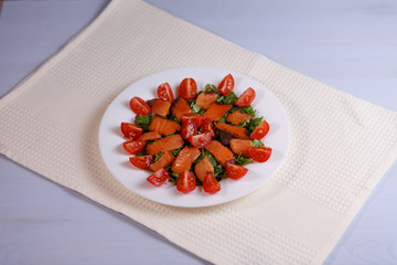 Greens, tomatoes, fish, cheese and sauce salad on a white plate on a white background.
