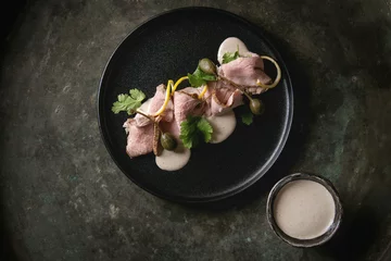 Zelfklevend Fotobehang Vitello tonnato italian dish. Thin sliced veal with tuna sauce, capers and coriander served on black plate over old dark metal background. Top view, space © Natasha Breen