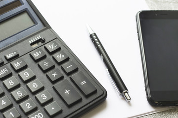 Business, Work, Counting Concept. A calculator, pen and a black smartphone on a white paper, close up