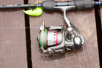 Modern Fishing Rod With Reel With Water Drops From Rain On Wooden Pier On Pond On Fishing Outdoor Close Up.