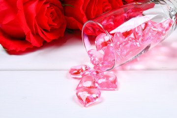 Champagne glasses filled with hearts surrounded by red roses on a white wooden table. Template for Valentine's Day.