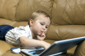 little boy is playing on the teaching computer at home on the couch