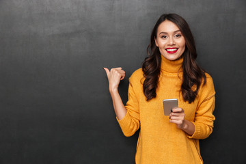 Smiling brunette woman in sweater holding smartphone