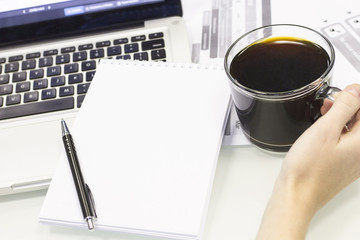 Business, Finance, Analysis concept. A workplace with a laptop computer, a notebook, a hand holding a cup of coffee