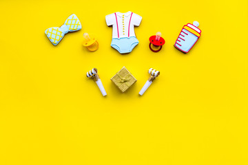 Celebrate birthday of a little baby. Cookies in shape of accesssories for child and gift box on yellow background top view copy space