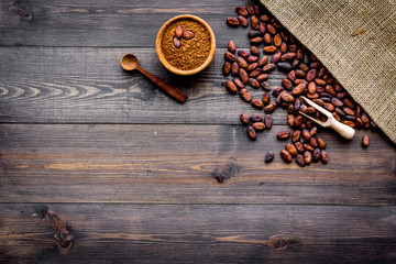 Cocoa powder near cocoa beans and canvas on dark wooden background top view copy space