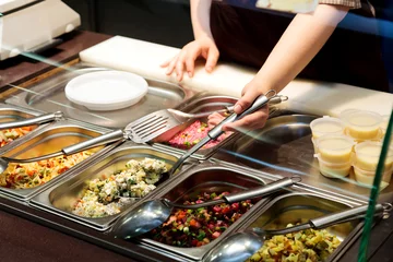 Behang Assortiment Dienbladen met gekookt voedsel op showcase in cafetaria. Saladevariatie bij een buffet
