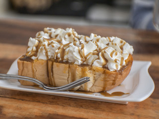 Toasted bread, whipped cream and caramel sauce are placed on a wooden table in cafe.