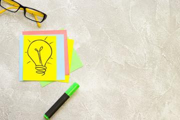 New Idea Creativity Business Concept with a copy space, computer glasses, colored paper, a text highlighter and a light bulb image on a grey concrete background, flat lay, top view