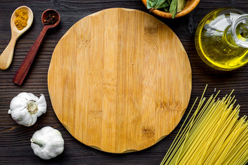 In restaurant. Mock up for menu or recipe. Wooden cutting board near ingredients. Raw pasta, oil, garlic, spices on dark wooden background top view
