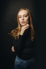 Naklejka premium Sexy blonde girl posing in a black technical clotheth on a black background. Advertising Space
