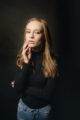Fototapeta premium Sexy blonde girl posing in a black technical clotheth on a black background. Advertising Space