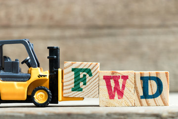 Toy yellow forklift hold letter block F to complete word FWD (Abbreviation of forward)on wood...
