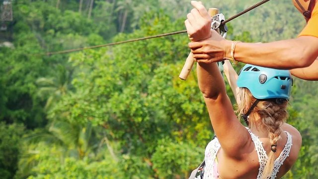 Young happy woman sliding on high speed zipline rope above beautiful tropic forest. slow motion. 1920x1080