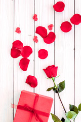 Prepare the prsesnts or surprise for Valentine's day. Red gift box near red rose and petals on white wooden background top view