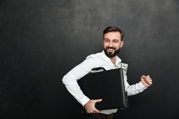 Funny picture of lucky man holding black briefcase full of dollar banknotes inside, isolated over...