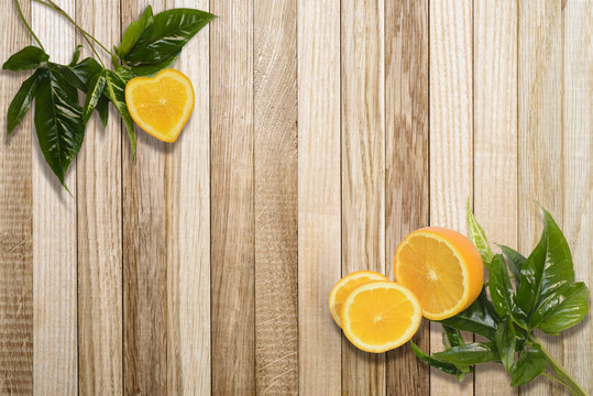 Oranges on a cut one of which in the form of heart with bright green original leaves isolated on a table of boards