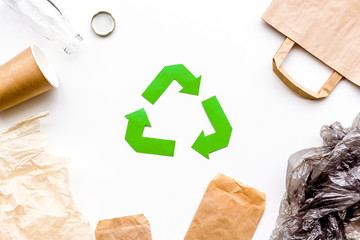 Sorting waste and recycle. Green paper recycling sign among waste paper, plastic, glass, polyethylene on white background top view