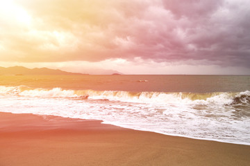 storm with big waves in the sun rays on the seashore with mountains on the background
