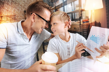 Close people. Positive emotional man in glasses looking happy while touching foreheads with his smiling son and sitting at the table with documents