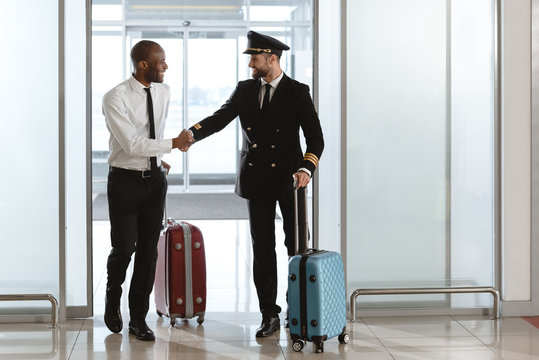 happy handsome pilot handshaking with young businessman at departure area of airport