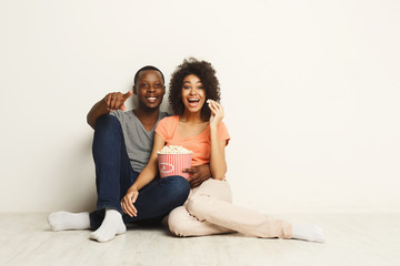 Fototapeta na wymiar Smiling black couple wathing movie at home on the floor