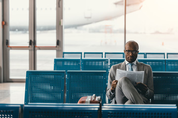 serious businessman reading newspaper waiting for flight at airport lobby