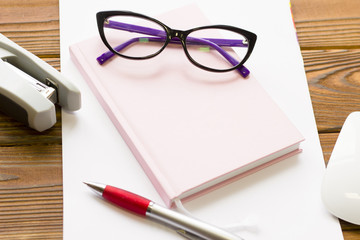 Business Office Workplace Concept with stylish computer glasses on a pink planner and stationary, close up, copy space