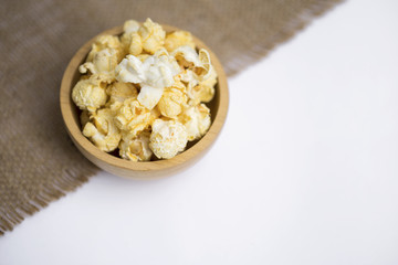 Popcorn in round wooden bowl on hessian fabric with space on white background, movie night snack