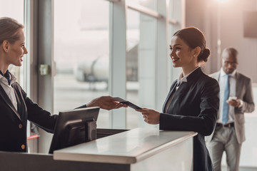 smiling young businesswoman giving passport and ticket to staff at airport check in counter