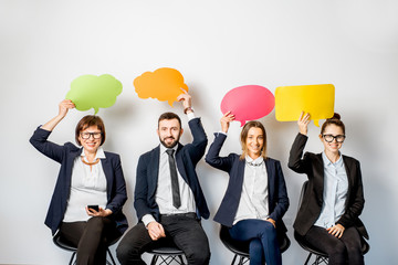 Business people holding colorful bubbles above the head sitting in a row on the white background