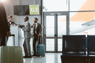 businessmen standing at airport reception to buy tickets while colleague walking to them
