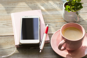 Stylish Business Office or Home Workplace Concept with cappuccino in a pink cup,a planner, smartphone and a plant in a pot on a light wooden table, close up