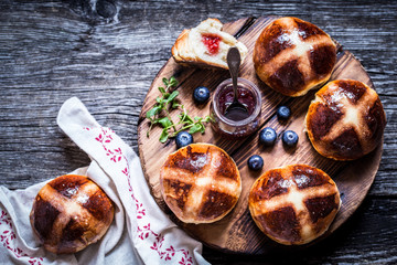 Easter hot cross buns on a wooden background with a jar of jam and fresh berries blueberry rustic
