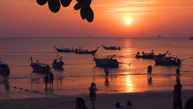 Thai beach at sunset with a lot Thai long tail boats and people silhouettes 