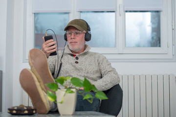 mature man with cap in headphones listening to music at home