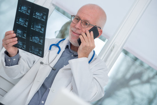 Mature doctor looking at x-ray picture and using  telephone